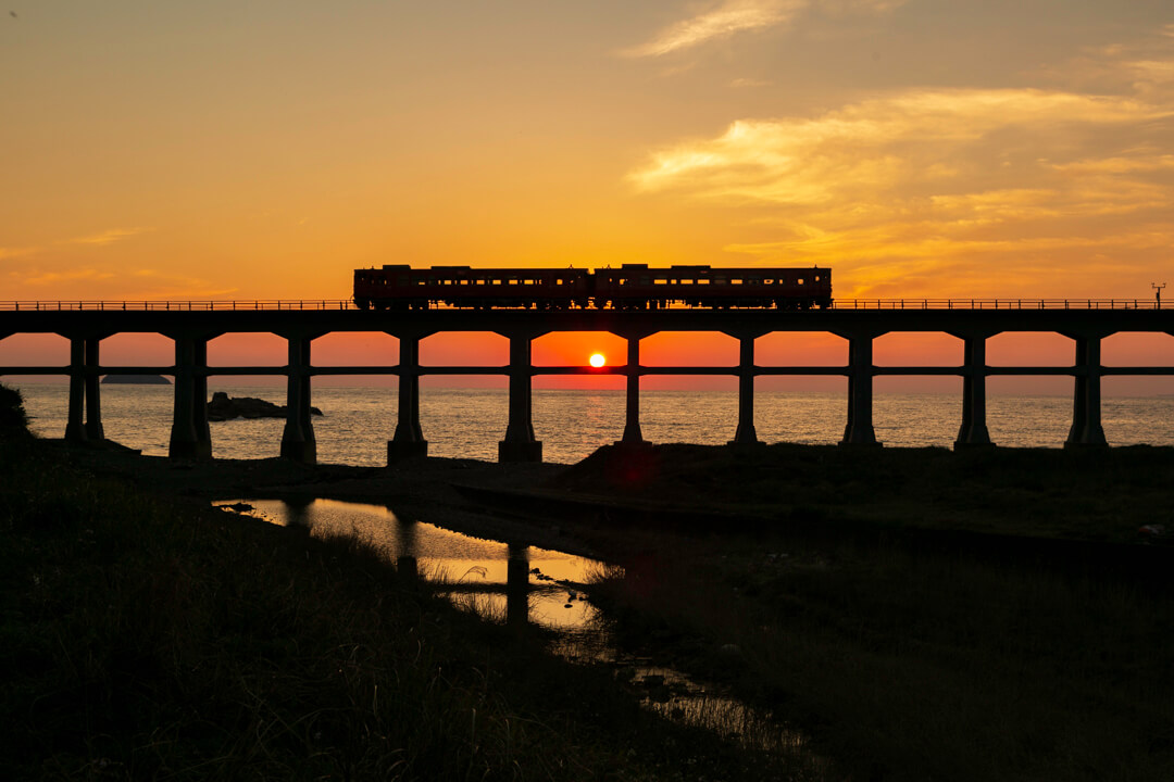夕日を背に走る列車と惣郷川橋梁の写真