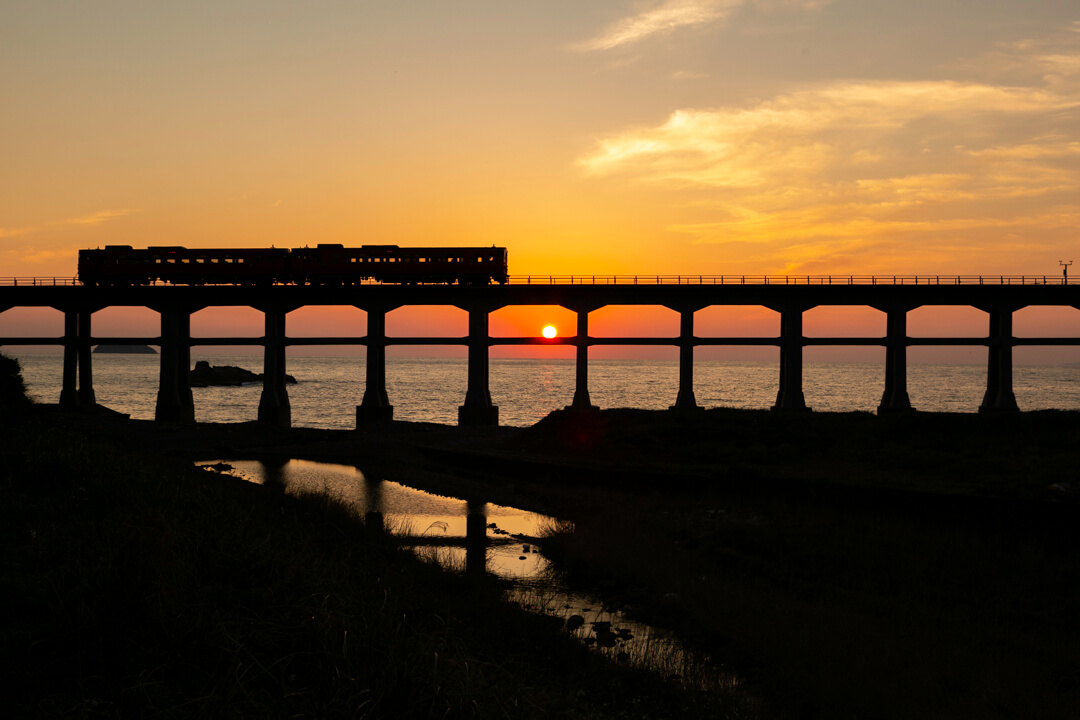 夕日を背に走る列車と惣郷川橋梁の写真